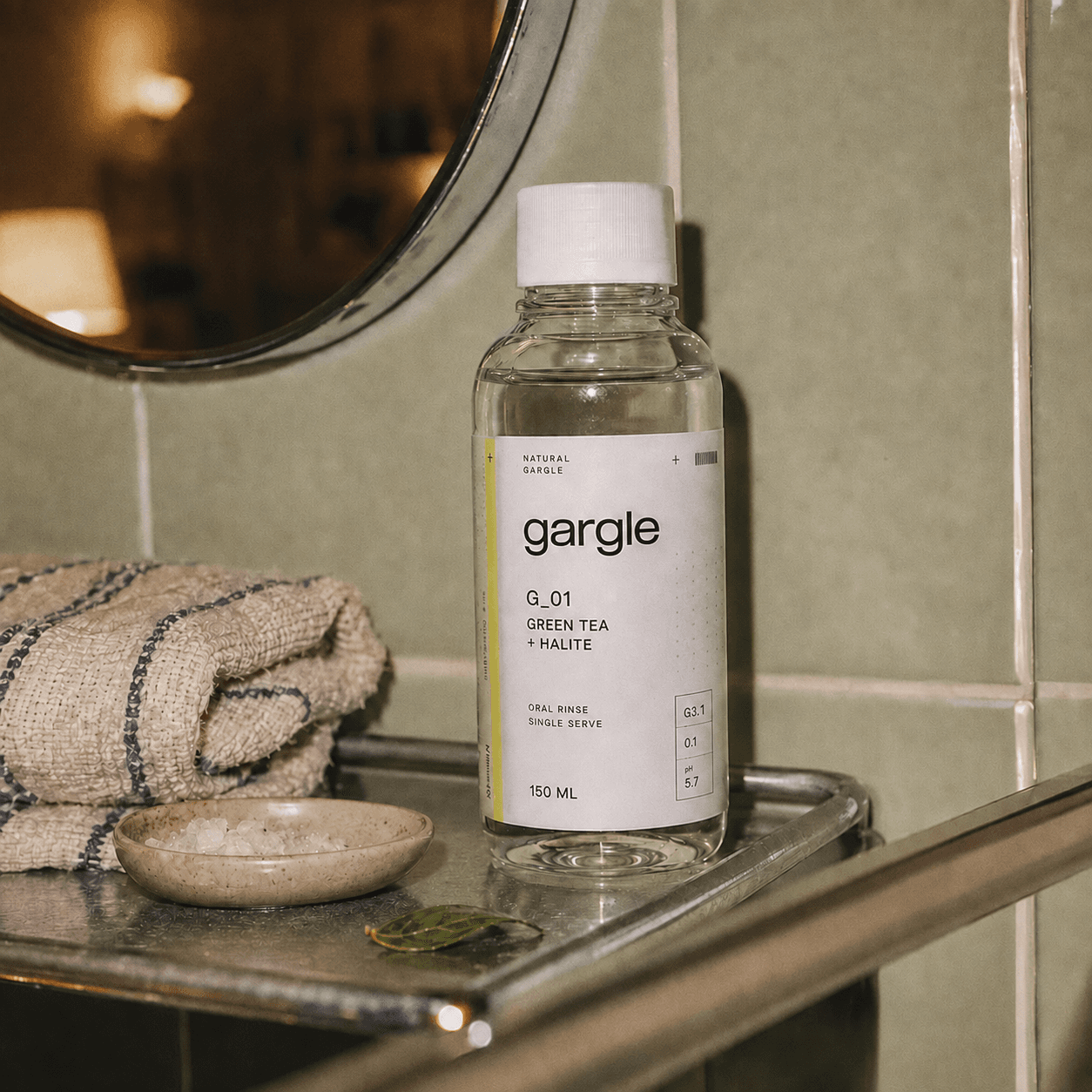 Gargle Green Tea + Halite bottle resting on a chrome shelf in a soft, sage-tiled bathroom.