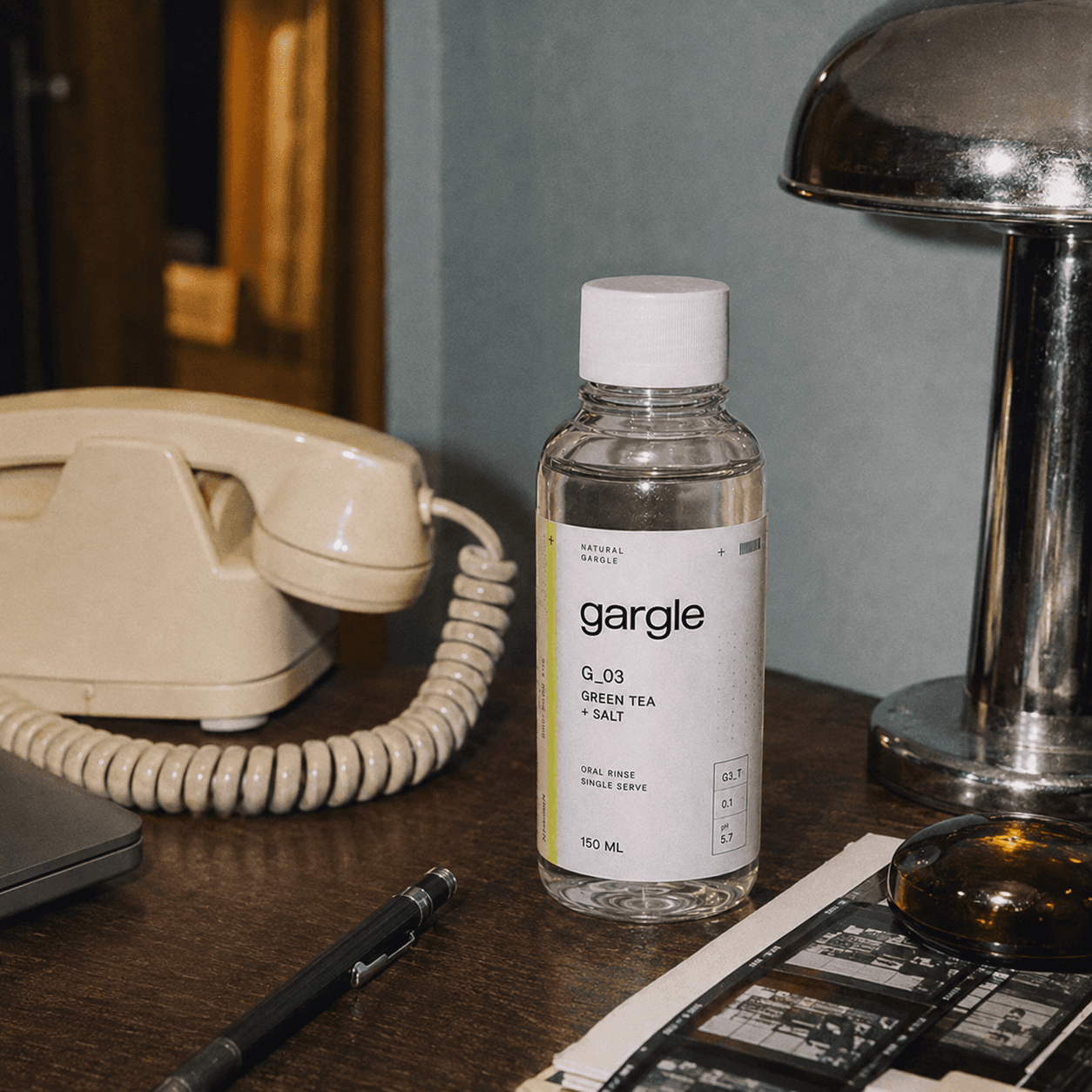 The Gargle bottle on a wooden desk beside a vintage lamp and a rotary telephone.